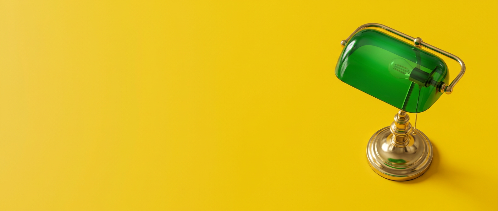 Abajur clássico banqueiro com cúpula verde e base dourada sobre fundo amarelo